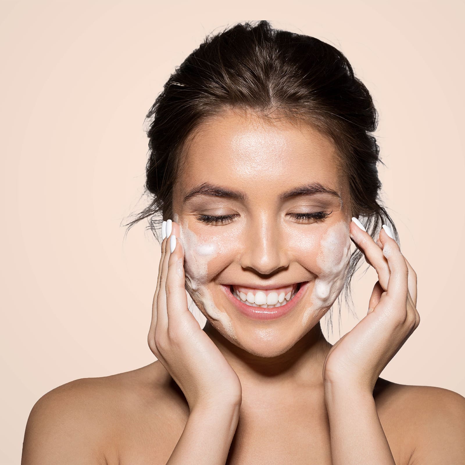 Young woman with a pink headband applying ODEON Face & Body Scrub (Strawberry & Aloe Vera) on her shoulder, smiling softly with closed eyes, showcasing smooth and radiant skin