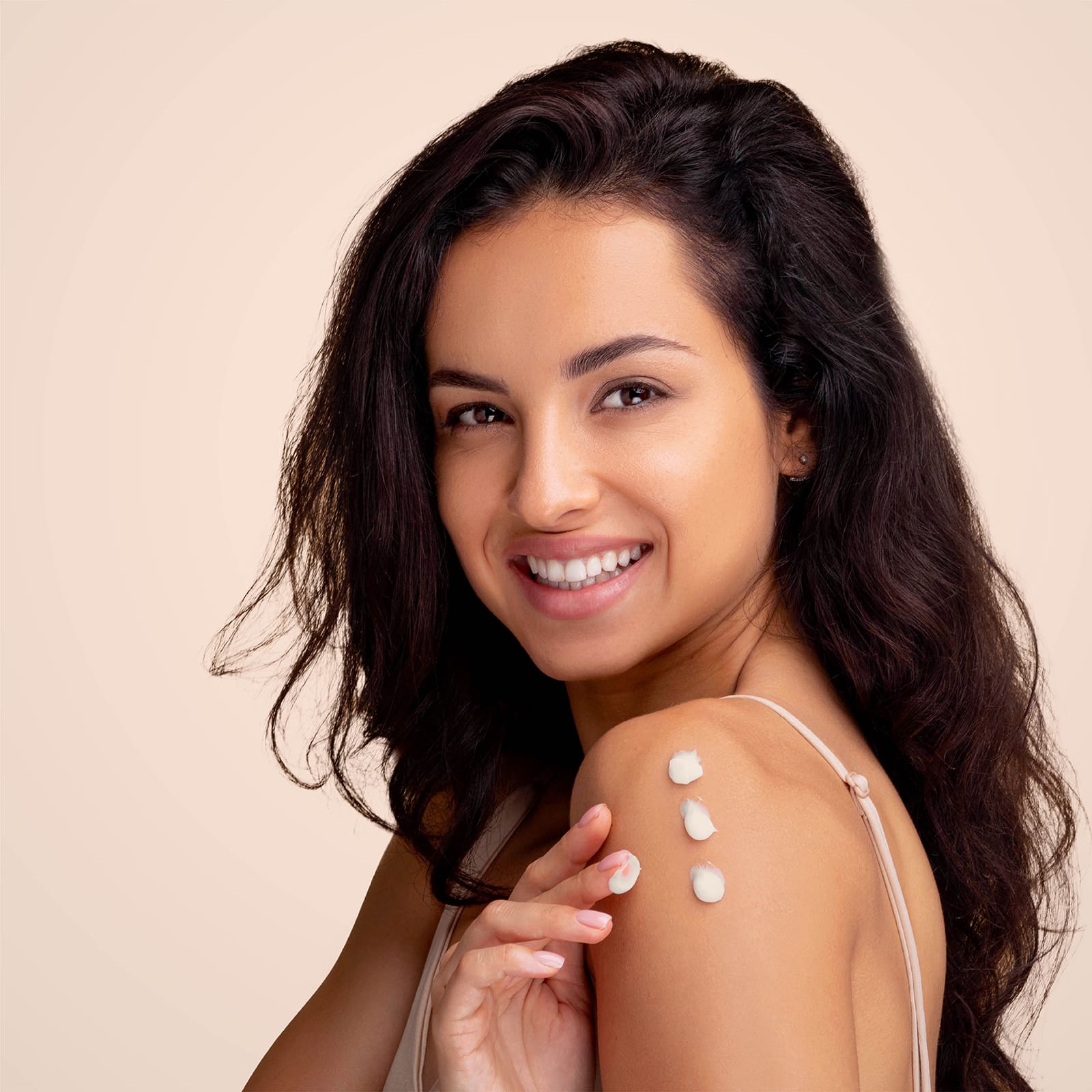 Smiling woman applying skincare lotion on her shoulder with four dots of cream on her skin, promoting healthy and glowing skin care routine