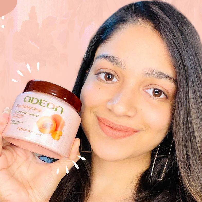 Smiling woman holding Odeon Face & Body Scrub with Apricot & Almond, showcasing the product for natural nourishment and 100% natural exfoliants against a peach-toned background